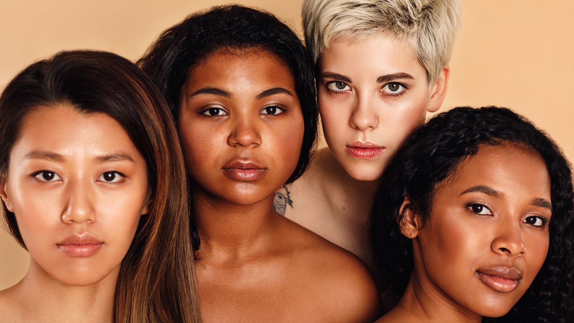 Four people with different skin tones photographed together against a warm studio backdrop.